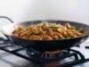 A Beginner’s Guide to Carbon Steel Woks: Introduction and Seasoning Tips Carbon steel wok with dark patina cooking stir fry on high heat gas burner - ChopChic.com