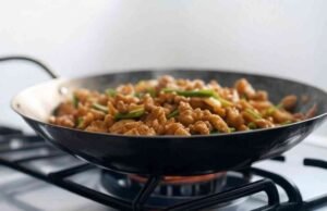 A Beginner’s Guide to Carbon Steel Woks: Introduction and Seasoning Tips Carbon steel wok with dark patina cooking stir fry on high heat gas burner - ChopChic.com