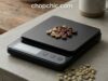 Choosing the Right Material for Your Coffee Scale Surface _A close-up view of a sleek, stainless steel coffee scale easily repelling a splash of dark espresso, demonstrating the practical maintenance and durability advantages of metal over porous plastic or fragile glass surfaces.