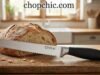 Orblue Serrated Bread Knife: Durability and Precision in a Single Sleek Design _A close-up of the Orblue one-piece stainless steel bread knife slicing through a crusty sourdough loaf, highlighting the seamless metal handle and wavy serrated edge designed to prevent squishing.