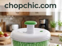 Farberware Pump Salad Spinner Review: The 1-Handed Fix A large, clear plastic Farberware 6.6-quart salad spinner resting on a wooden kitchen island, showing a single hand pushing down on the central vertical pump mechanism, causing the internal green colander basket to blur from high-speed rotation, with the built-in brake button visible on the lid.