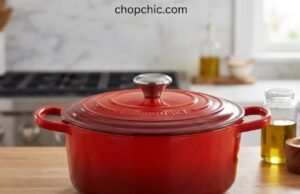 Le Creuset Dutch Oven Review: Why Bakers Pay a Premium A vibrant Cerise red Le Creuset Signature enameled cast iron Dutch oven sitting on a wooden cutting board, with its tight-fitting lid resting beside it to reveal a deeply browned, crusty sourdough boule resting inside the pristine light-sand interior.