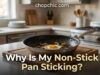 Why Is My Non-Stick Pan Sticking? (And How to Fix It) A heavily used non-stick skillet showing stubborn, burnt-on food residue, positioned on a kitchen counter next to a glass bowl of white vinegar and a measuring spoon of baking soda.