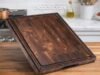 Sonder LA Alfred Review: Ultimate Walnut Wood Cutting Board A thick, dark walnut end-grain Sonder Los Angeles cutting board resting on a bright countertop, showcasing a high-end Japanese Santoku knife alongside the board's integrated sorting compartments and deep juice groove.