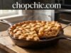 Lodge 9-Inch Cast Iron Pie Pan Review: The Physics of a Flaky Crust A detailed close-up photograph of a Lodge Cast Iron Pie Pan sitting on a rustic wooden table. A freshly baked deep-dish apple pie with a beautiful, professional golden lattice crust is inside the pan. A slice has been slightly lifted to reveal the flaky texture of the crust and the rich apple filling, emphasizing the heavy-duty seasoned cast iron construction. The setting is a warm kitchen with natural light. The text 'chopchic.com' is cleanly overlayed across the top center of the image.