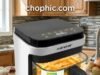 Transparent Cooking Dynamics: NutriChef 5.8 Quart Technical Review A technical product photograph of the NutriChef 5.8 Quart glass air fryer on a modern kitchen counter. The transparent glass fry bowl holds golden sweet potato fries. The heating pod shows a 1200W indicator, and a hand adjusts the ergonomic handle, suggesting manageability. Heat waves are subtly illustrated rising from the glass to emphasize thermal activity. A watermark is at the top of the image.